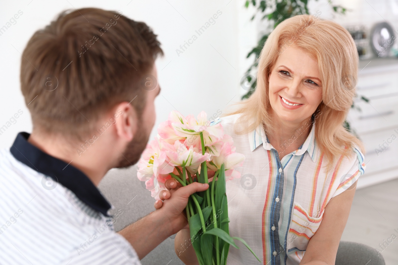 Photo of Young man congratulating his mature mom at home. Happy Mother's Day
