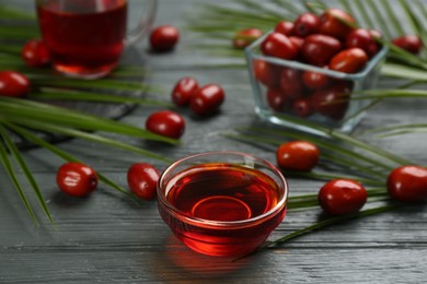 Photo of Palm oil in glass bowl, tropical leaf and fruits on grey wooden table