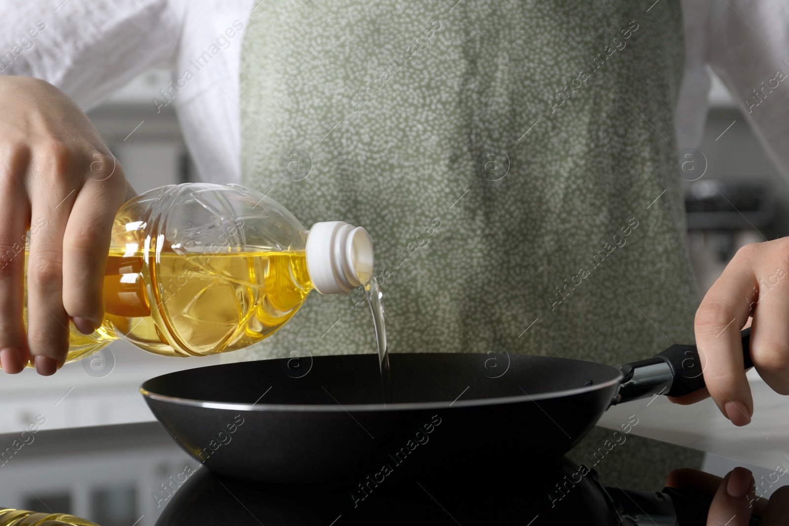 Photo of Woman pouring cooking oil from bottle into frying pan on stove, closeup