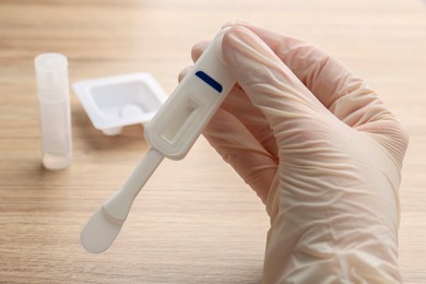 Photo of Woman holding disposable express test above wooden table, closeup