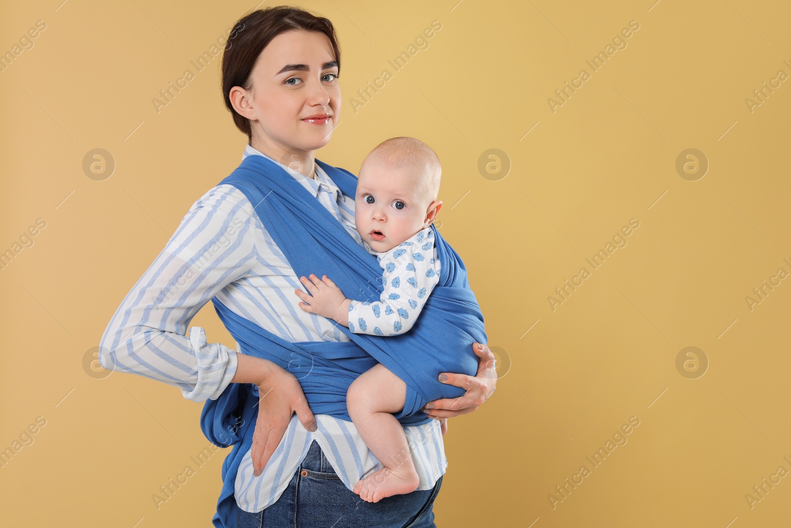 Photo of Mother holding her child in sling (baby carrier) on beige background. Space for text