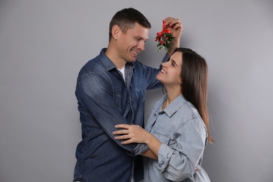 Happy couple standing under mistletoe bunch on grey background