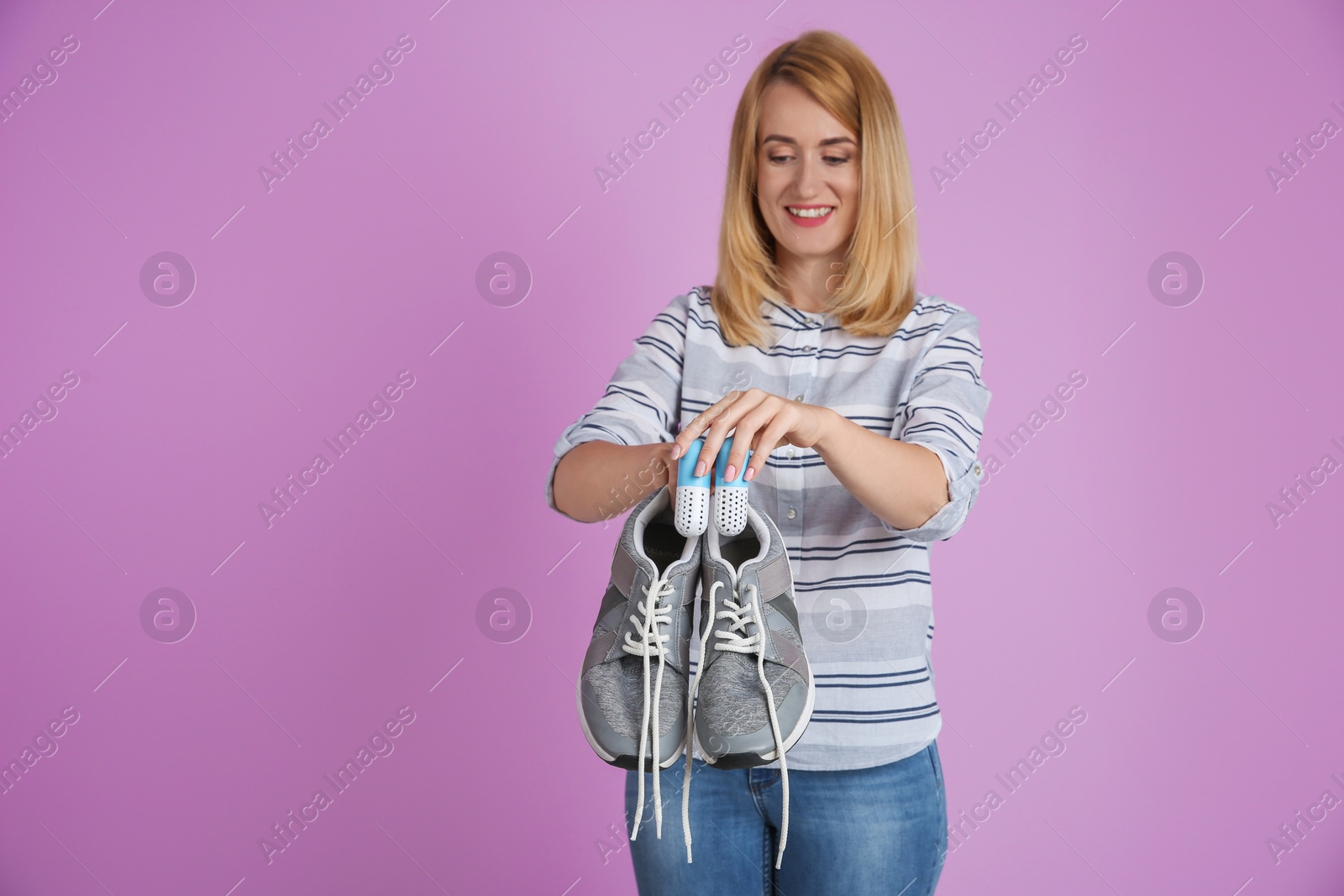 Photo of Young woman putting capsule air fresheners in shoes on color background