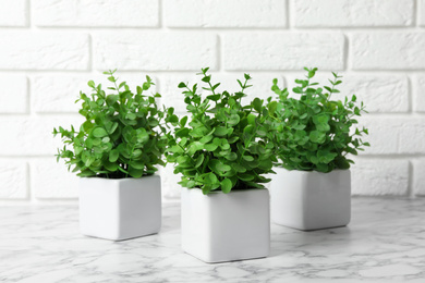 Photo of Beautiful artificial plants in flower pots on white marble table near brick wall