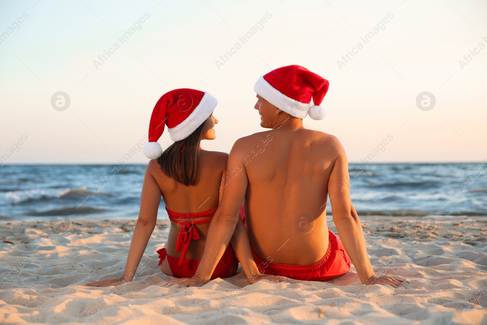 Photo of Lovely couple with Santa hats together on beach, back view. Christmas vacation