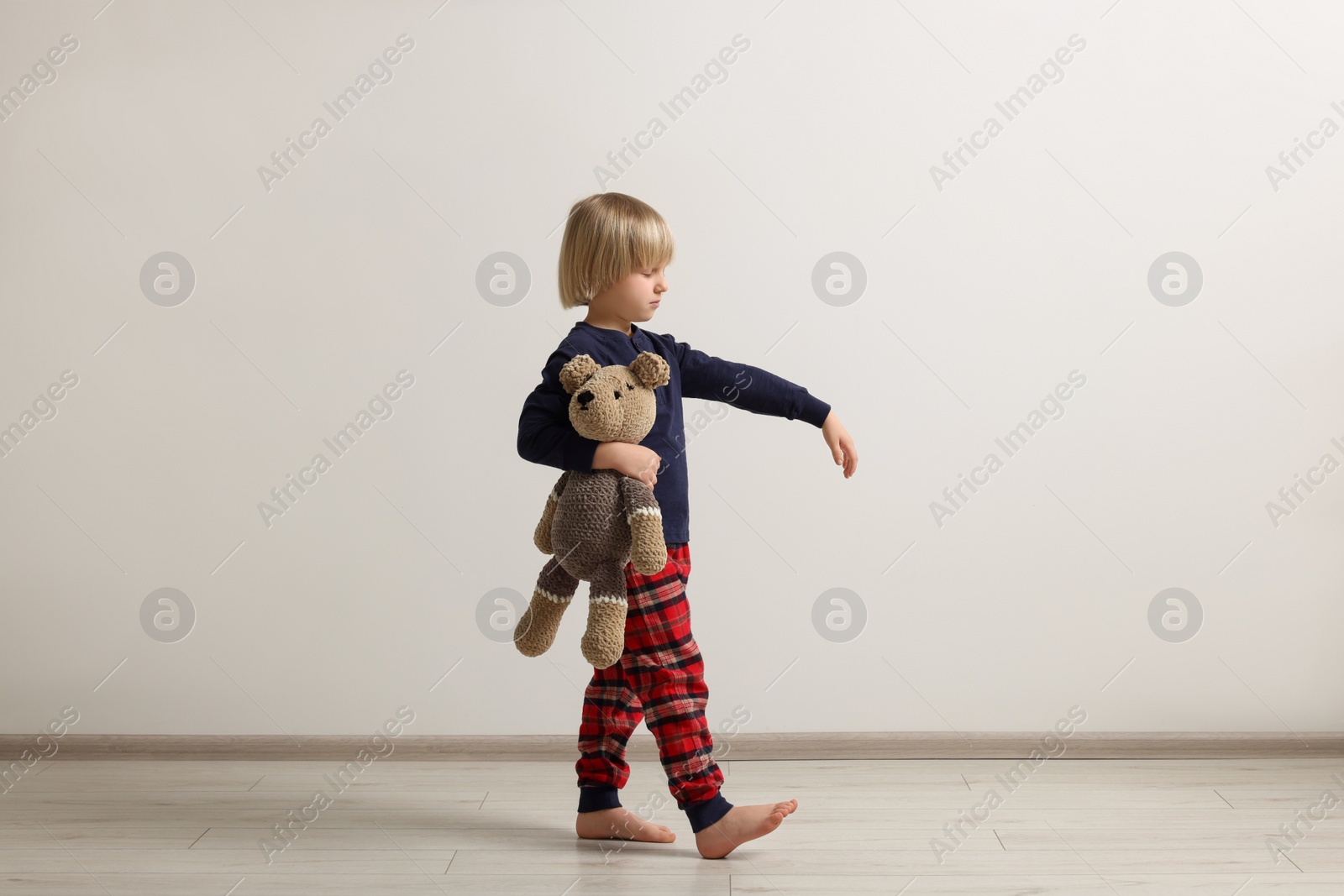 Photo of Boy in pajamas with toy bear sleepwalking indoors