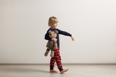Photo of Boy in pajamas with toy bear sleepwalking indoors