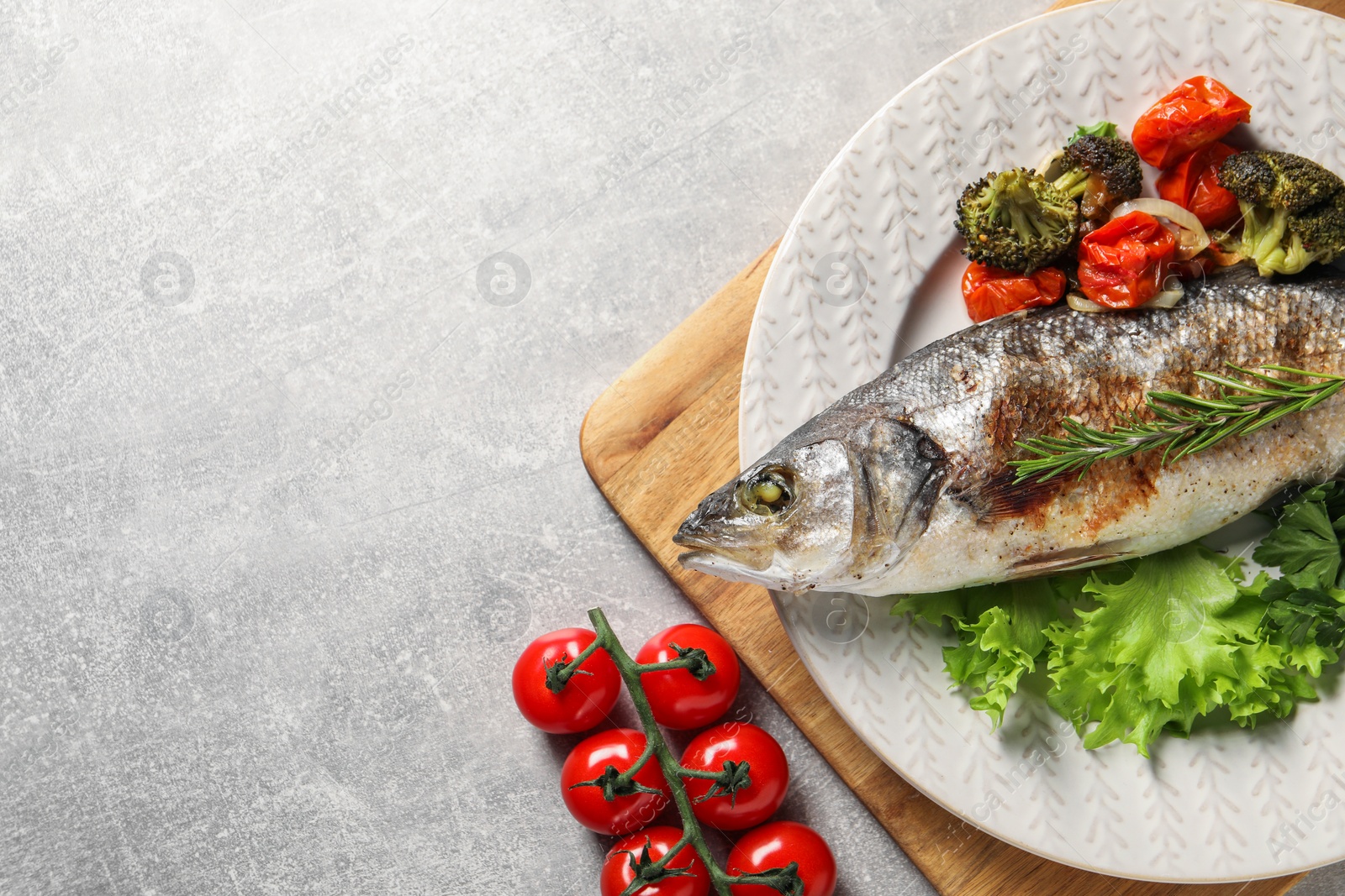 Photo of Delicious baked fish and vegetables on light grey table, top view. Space for text