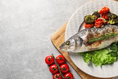 Photo of Delicious baked fish and vegetables on light grey table, top view. Space for text