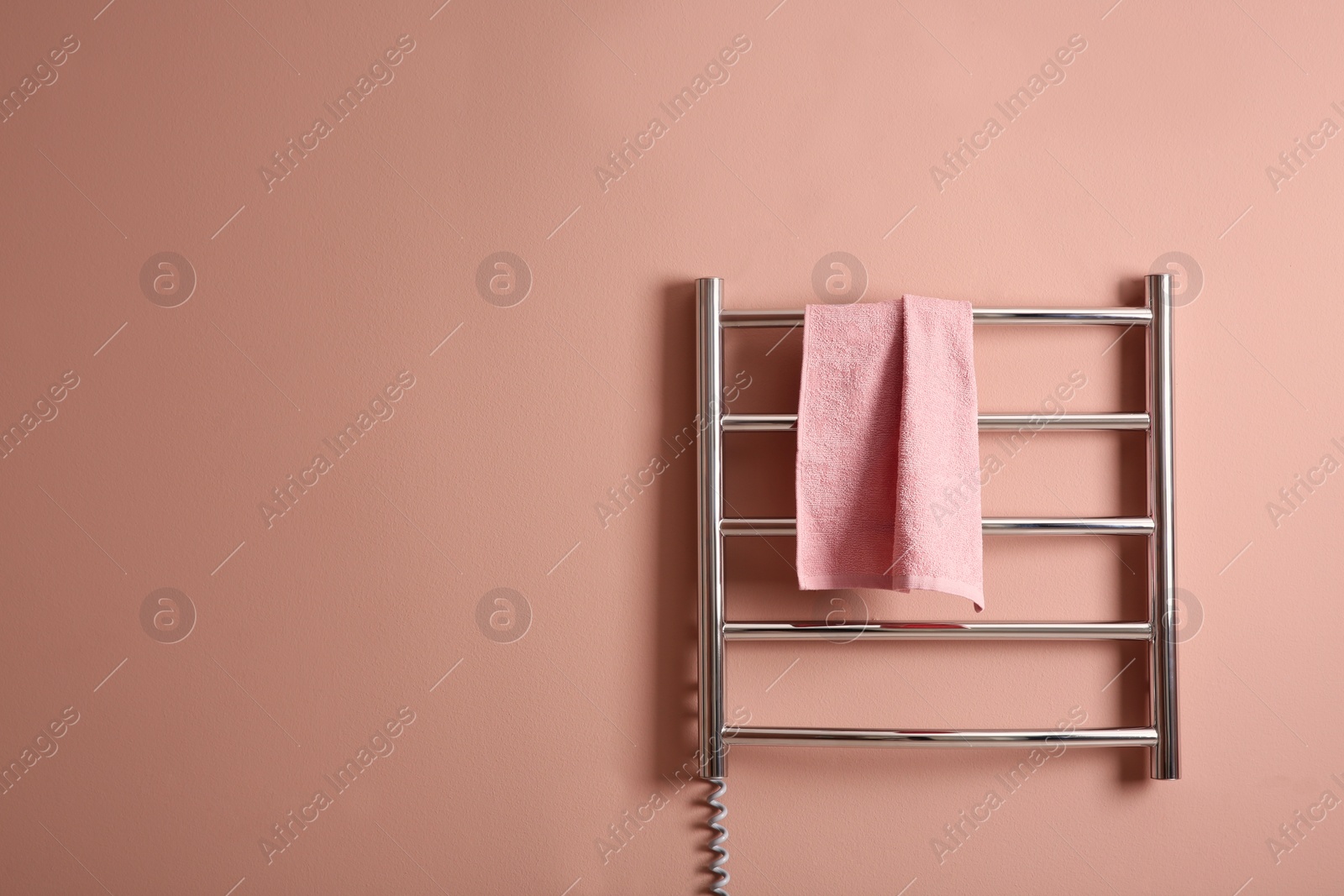 Photo of Modern heated towel rail with warm soft towel on light pink wall. Space for text