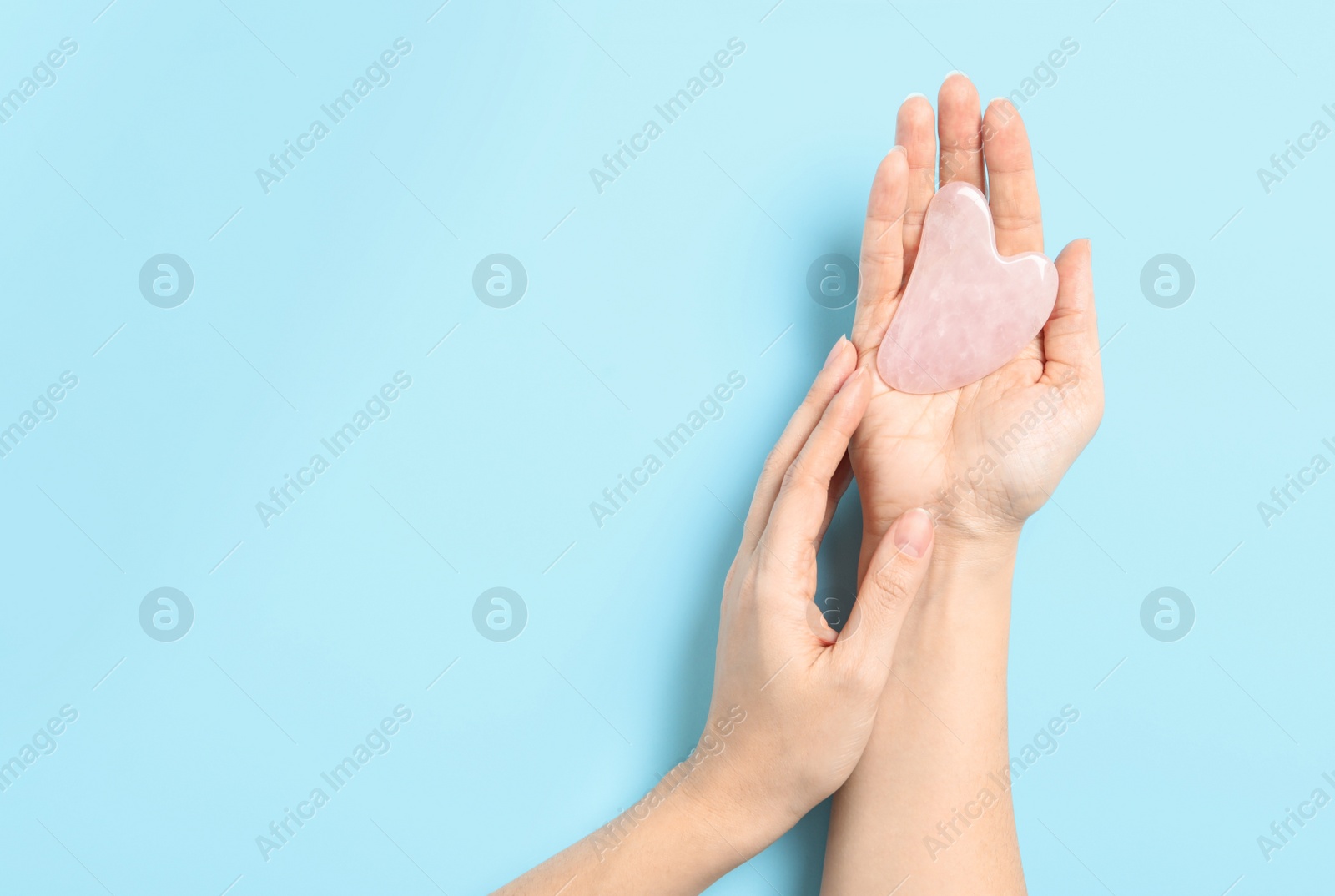 Photo of Woman with rose quartz gua sha tool on light blue background, closeup. Space for text