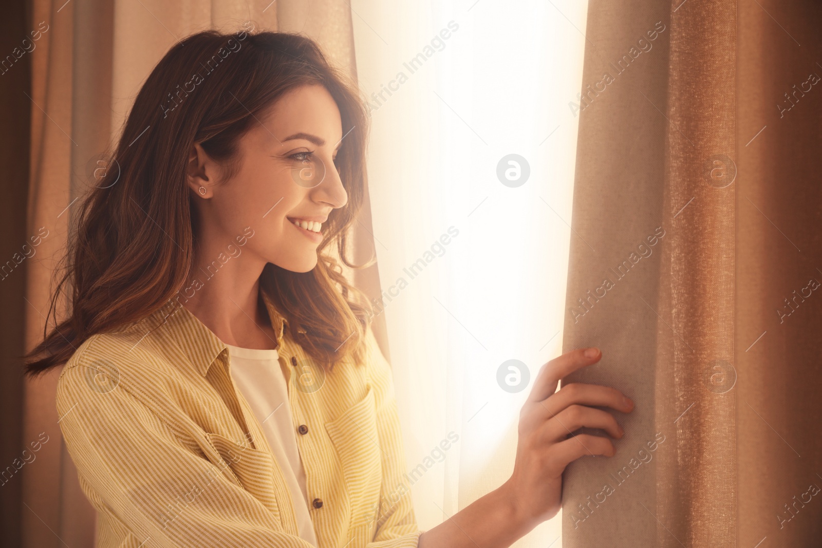 Image of Happy woman opening window curtains at home