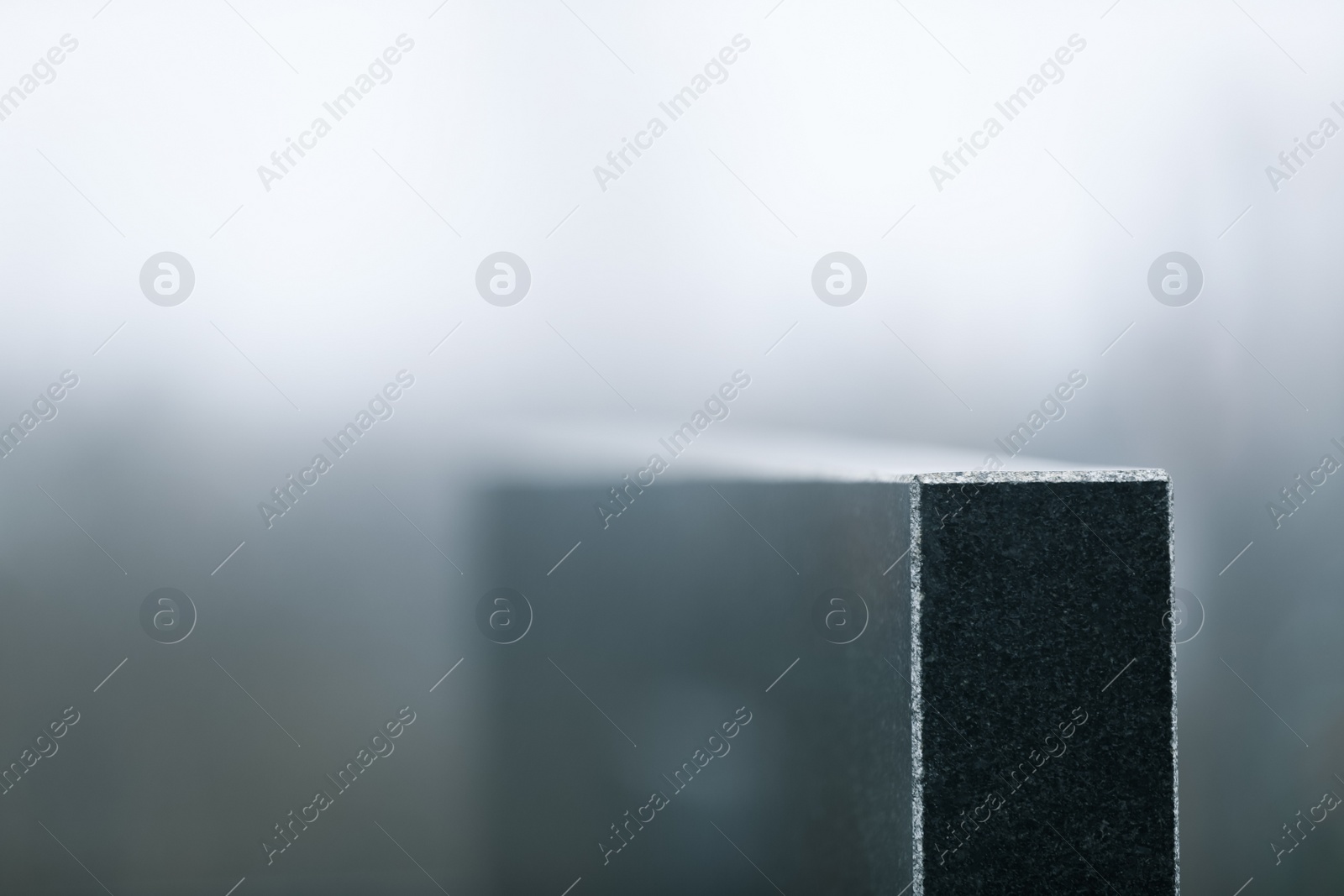 Photo of Black granite tombstone on blurred background, closeup with space for text. Funeral ceremony