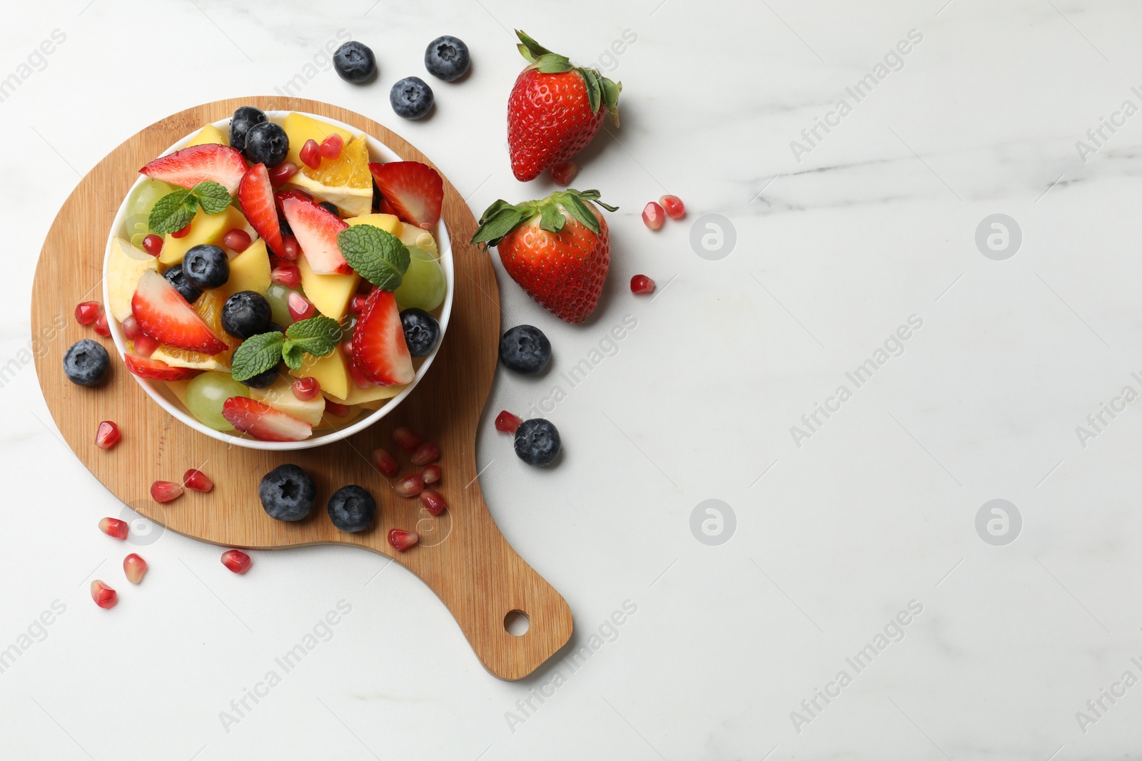 Photo of Tasty fruit salad in bowl and ingredients on white table, flat lay. Space for text