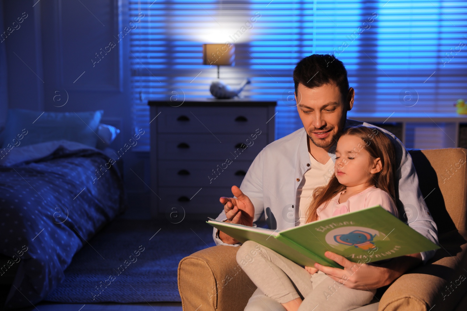 Photo of Father reading bedtime story to his daughter at home