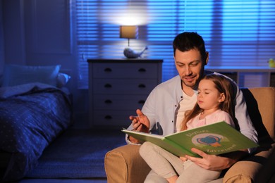 Photo of Father reading bedtime story to his daughter at home