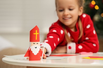 Cute little girl with paper Saint Nicholas toy at home, focus on hand