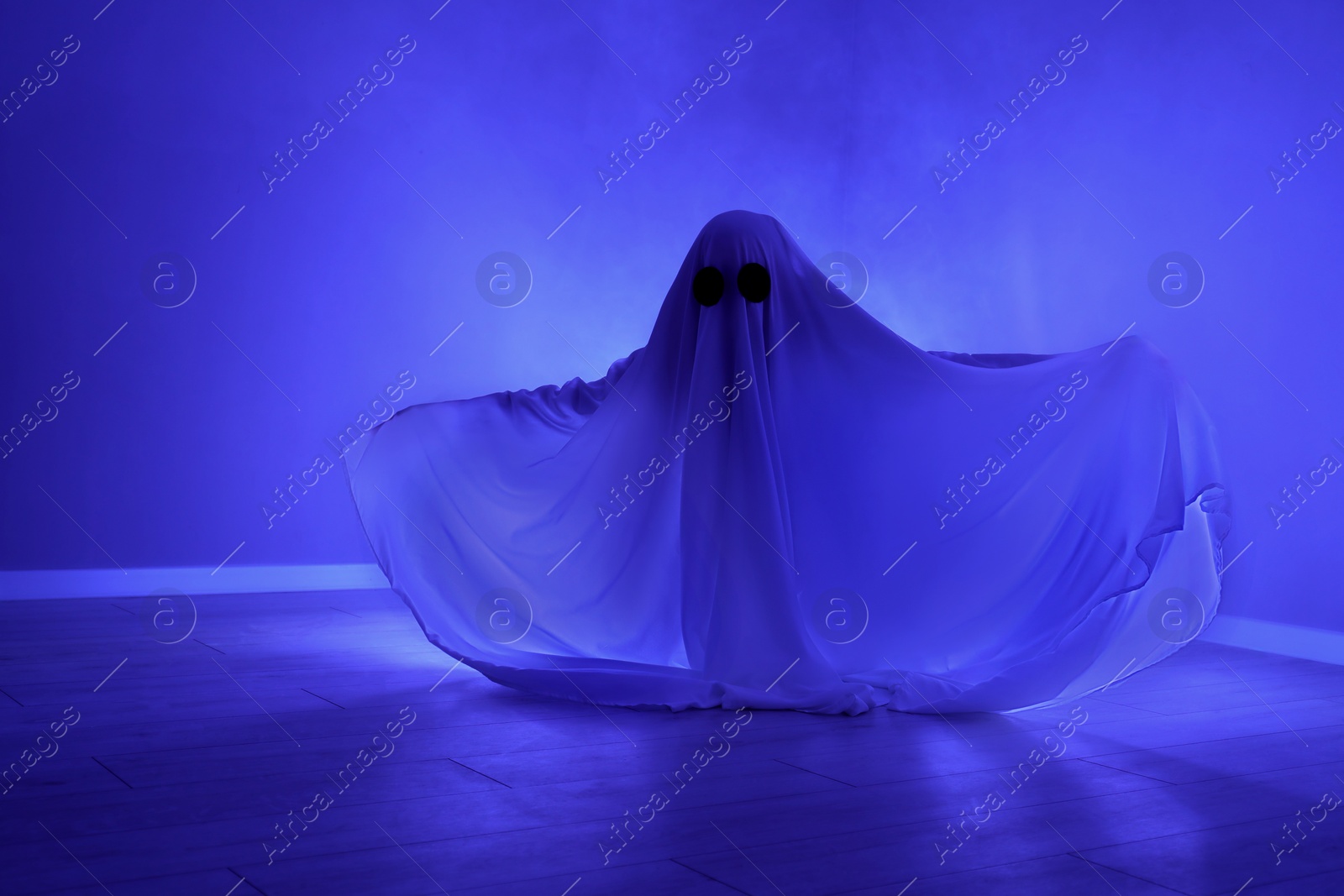 Photo of Creepy ghost. Woman covered with sheet in blue light