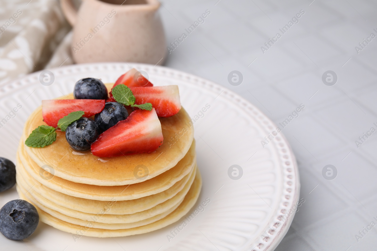 Photo of Delicious pancakes with strawberries, blueberries and mint served on white tiled table, closeup. Space for text