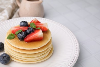 Delicious pancakes with strawberries, blueberries and mint served on white tiled table, closeup. Space for text