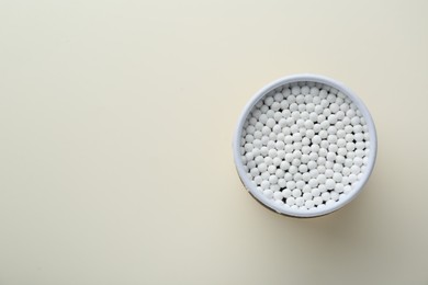 Container with new cotton buds on beige background, top view. Space for text