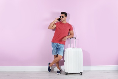 Photo of Young man with suitcase on color wall background