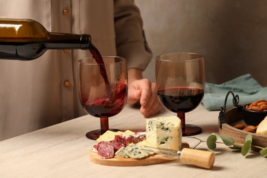 Photo of Woman pouring red wine into glass at wooden table, closeup