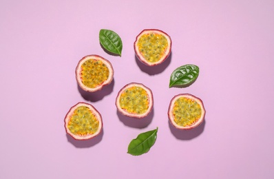 Photo of Halves of passion fruits (maracuyas) and green leaves on pink background, flat lay