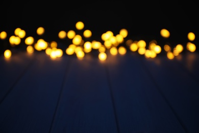 Blurred view of beautiful glowing lights, focus on blue wooden table. Space for text