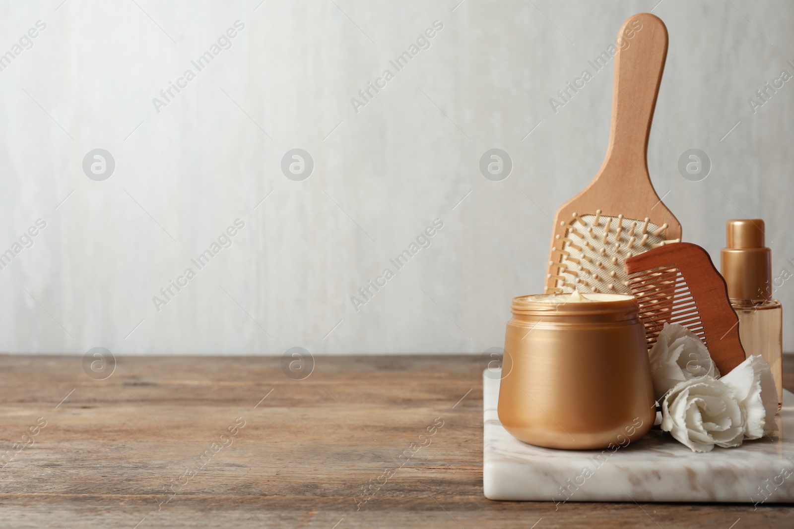 Photo of Different hair products, flowers and comb on wooden table. Space for text