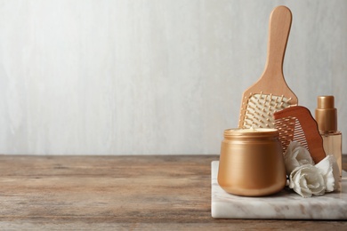 Different hair products, flowers and comb on wooden table. Space for text