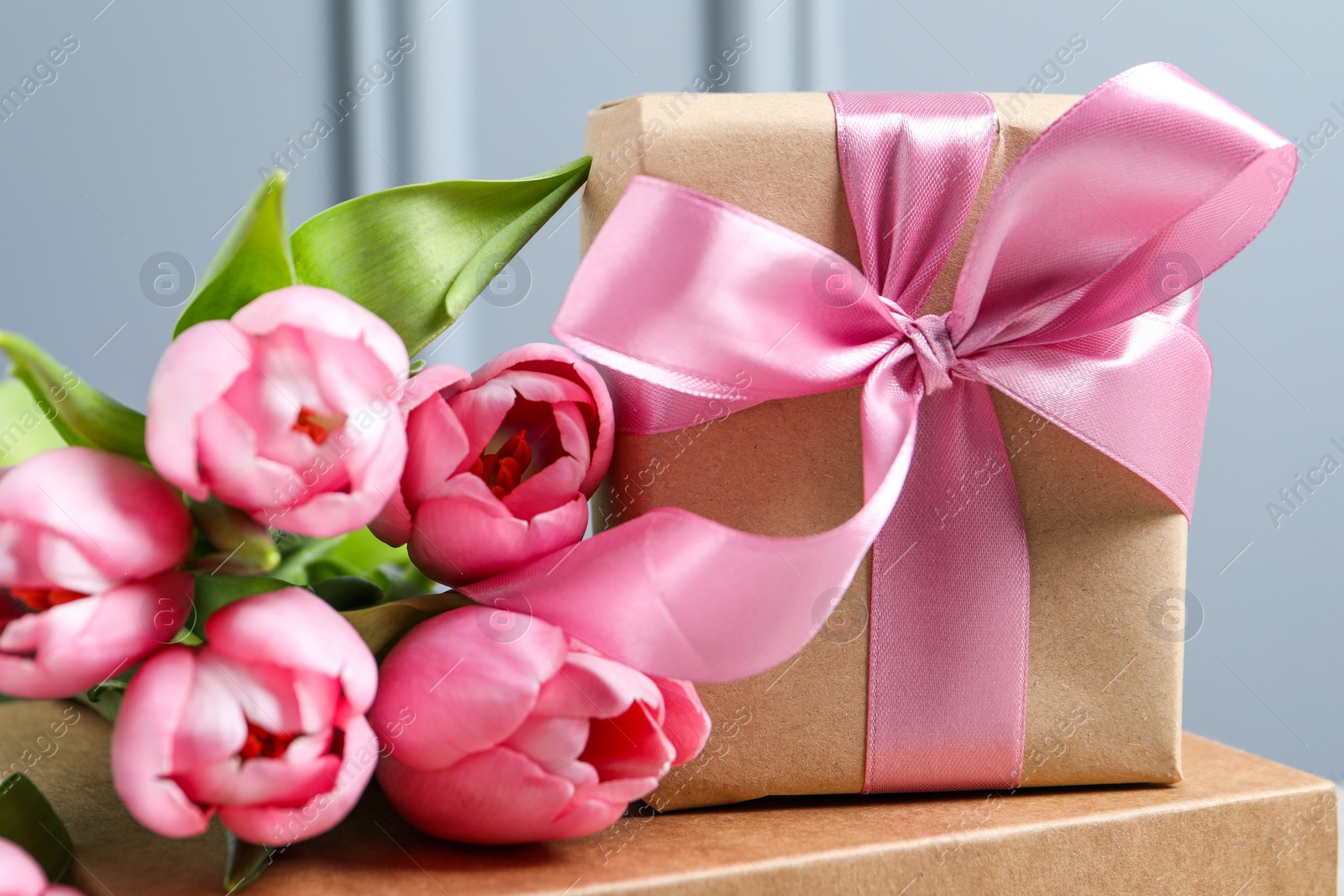 Photo of Beautiful gift box with bow and pink tulip flowers on grey background, closeup