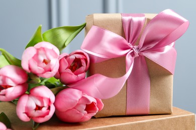 Photo of Beautiful gift box with bow and pink tulip flowers on grey background, closeup