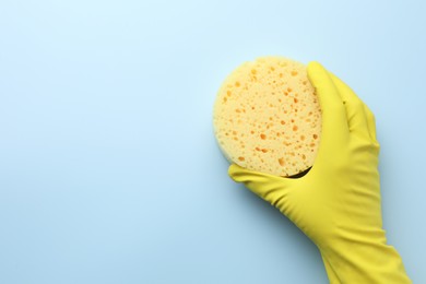 Photo of Cleaner in rubber glove holding new yellow sponge on light blue background, top view. Space for text