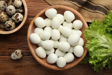 Unpeeled and peeled boiled quail eggs on wooden table, flat lay