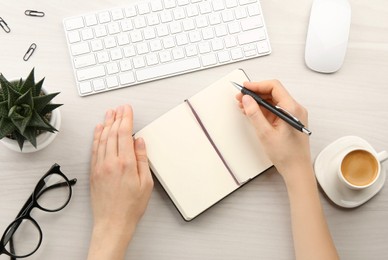 Photo of Woman writing in notebook at light wooden table, top view