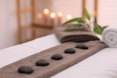 Photo of Towel with arranged spa stones on massage table in recreational center, closeup