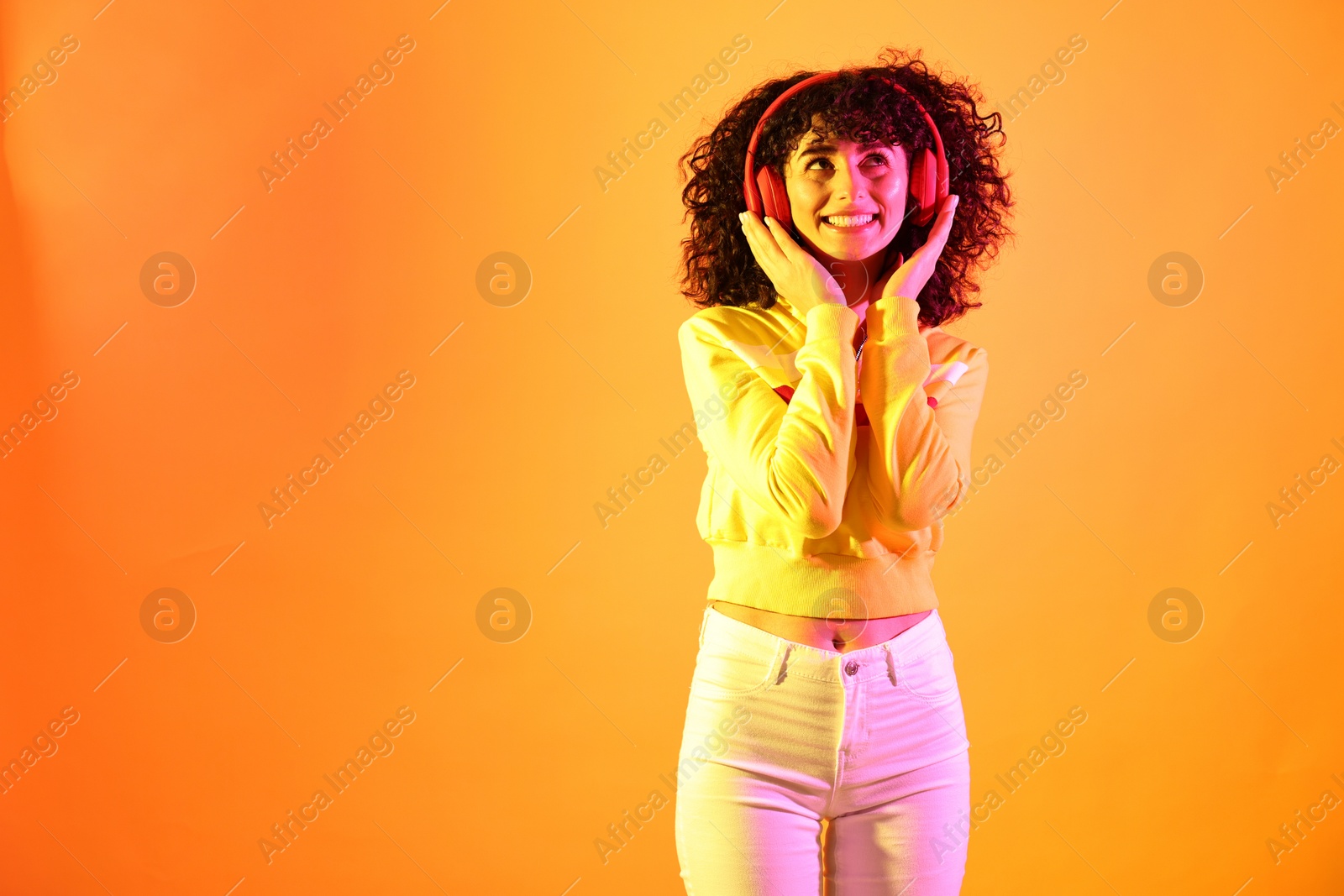 Photo of Beautiful young woman listening to music with headphones on color background in neon lights. Space for text