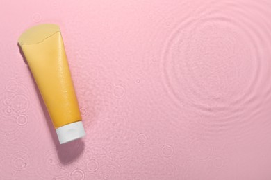 Photo of Tube of facial cleanser in water against pink background, top view. Space for text