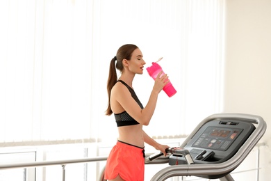 Athletic young woman drinking protein shake on running machine in gym