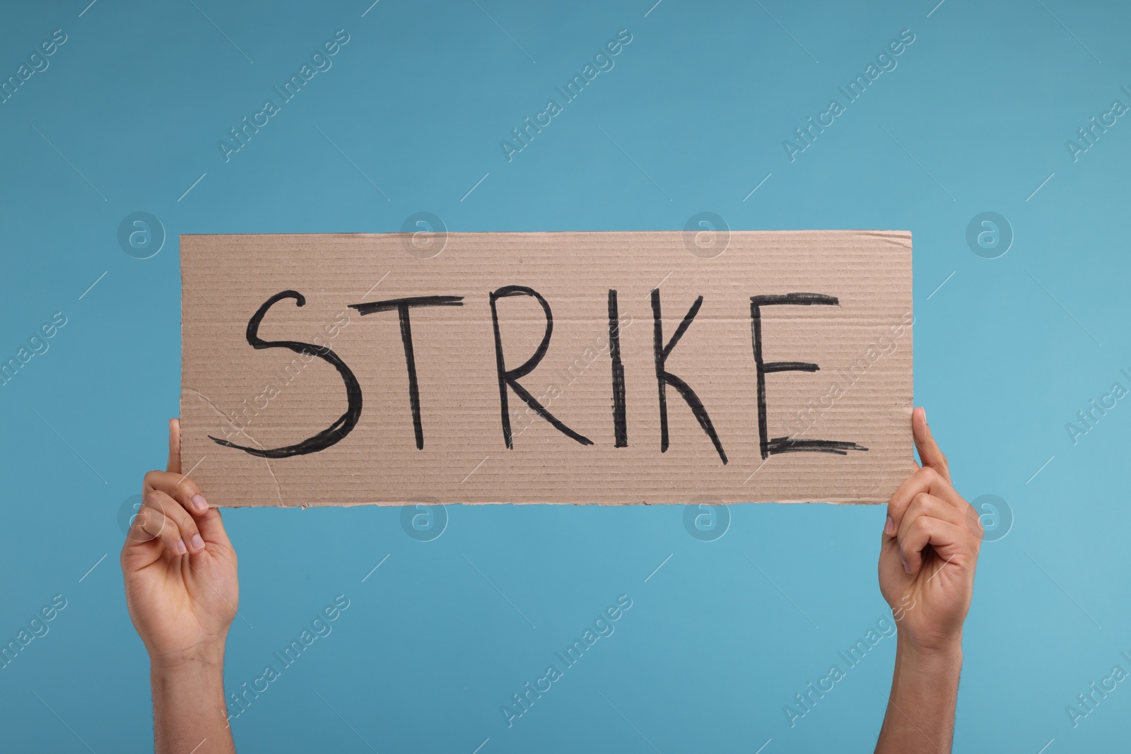 Photo of Man holding cardboard banner with word Strike on light blue background, closeup
