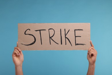 Man holding cardboard banner with word Strike on light blue background, closeup