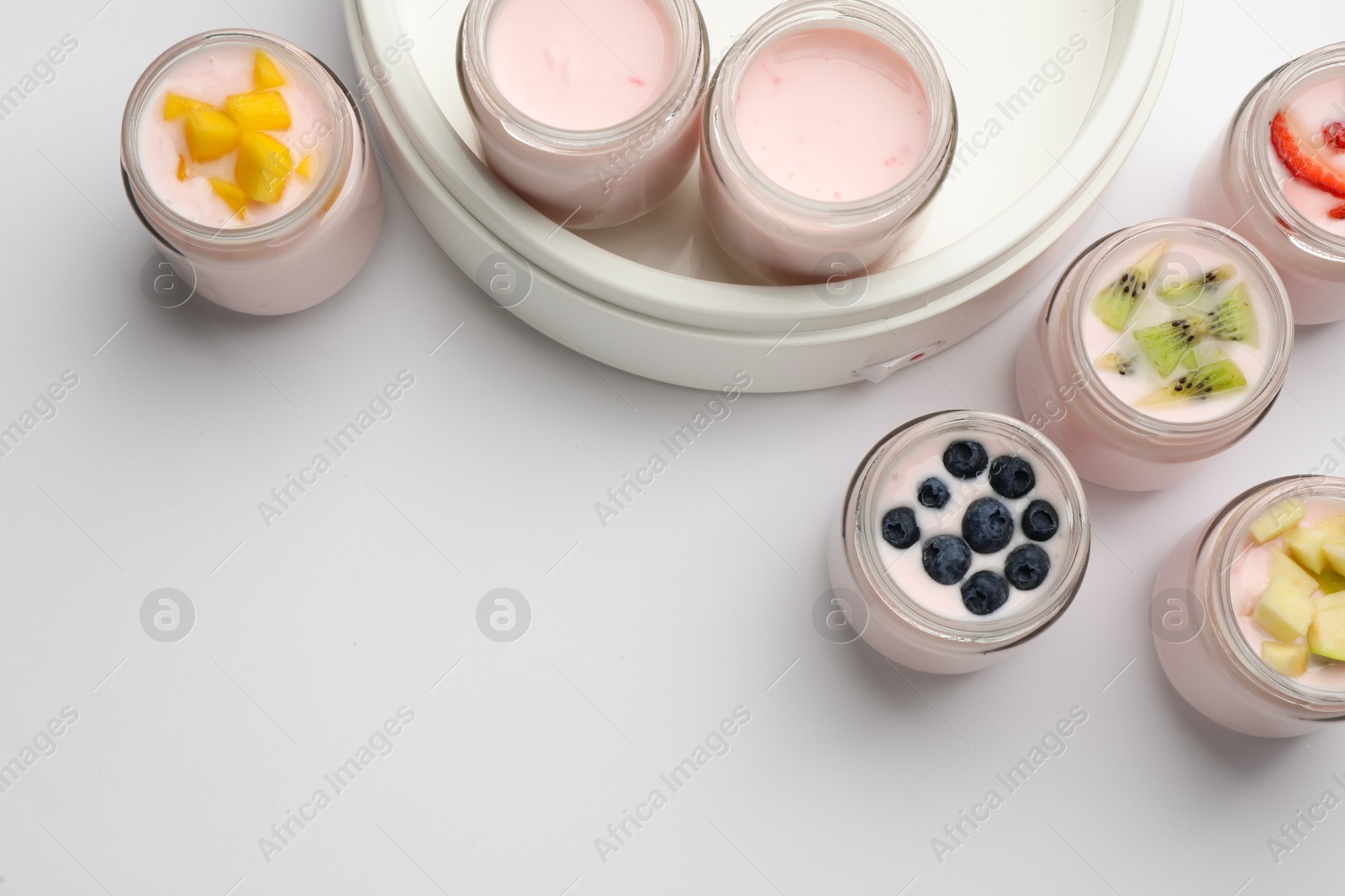 Photo of Tasty yogurt in glass jars and ingredients on white background, top view. Space for text