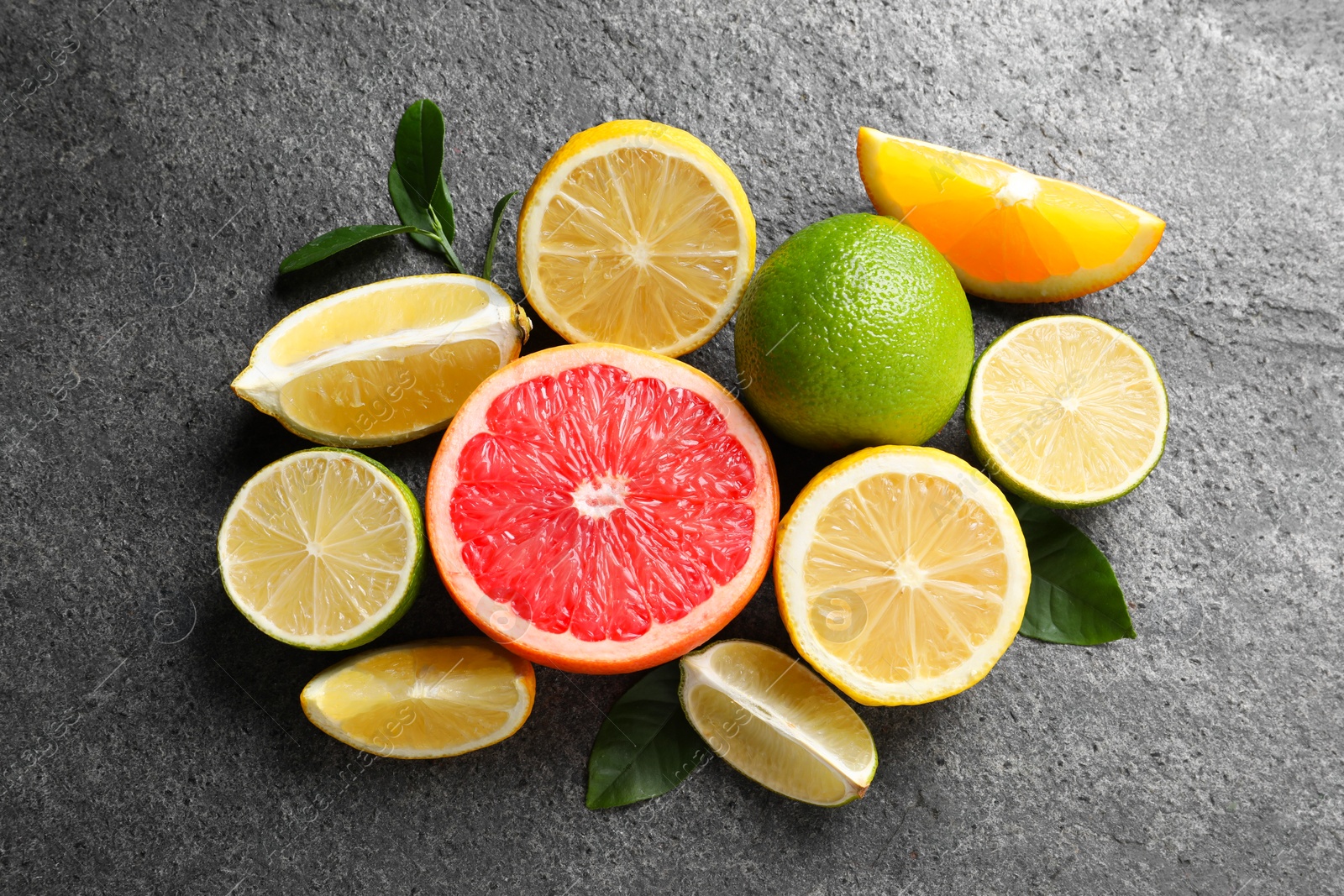 Photo of Different fresh citrus fruits and leaves on grey textured table, flat lay