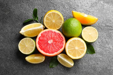 Photo of Different fresh citrus fruits and leaves on grey textured table, flat lay