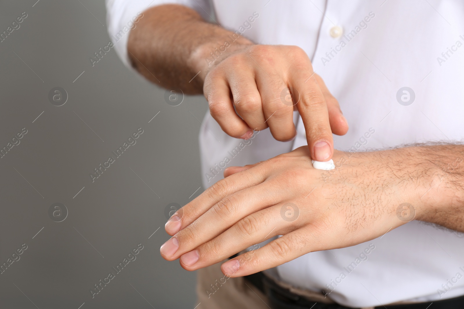 Photo of Man applying cream onto hand on grey background, closeup. Space for text