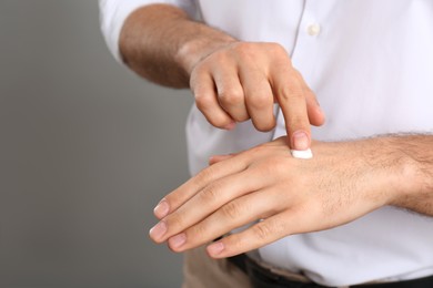 Photo of Man applying cream onto hand on grey background, closeup. Space for text