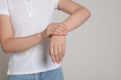 Woman suffering from pain in her hand on light grey background, closeup with space for text. Arthritis symptoms