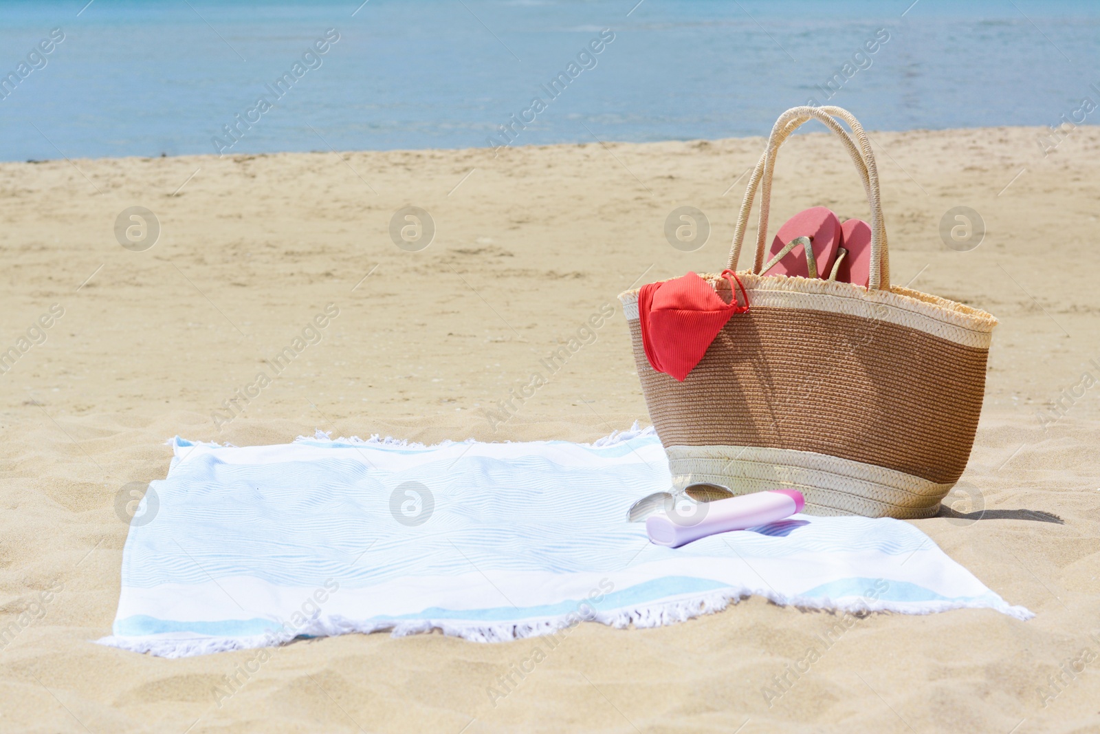 Photo of Light blue striped towel with bag, flip flops, sunglasses and sunblock on sandy beach