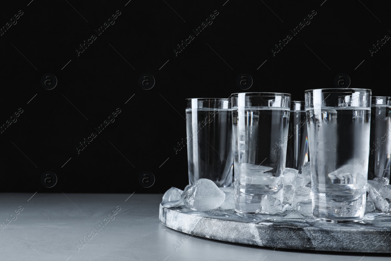 Photo of Vodka in shot glasses and ice on grey table. Space for text
